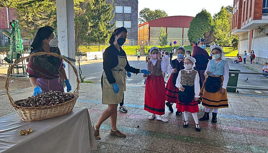 Tres de las madres “castañeras” repartiendo castañas a Lucía Valdés, Lucía  Bernardo, Jimena Vega y Sara González, vestidas de asturianas. | I. G. 