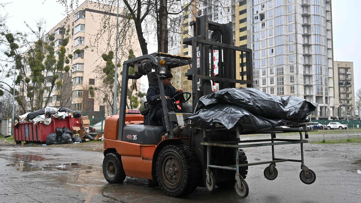 Un hombre conduce una carretilla elevadora mientras entrega bolsas que contienen cuerpos exhumados a un camión refrigerado en una morgue en Bucha, al noroeste de Kiev, el 22 de abril de 2022