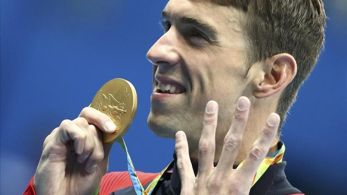 Phelps muestra su medalla señalando los cuatro oros que ha conseguido hasta ahora