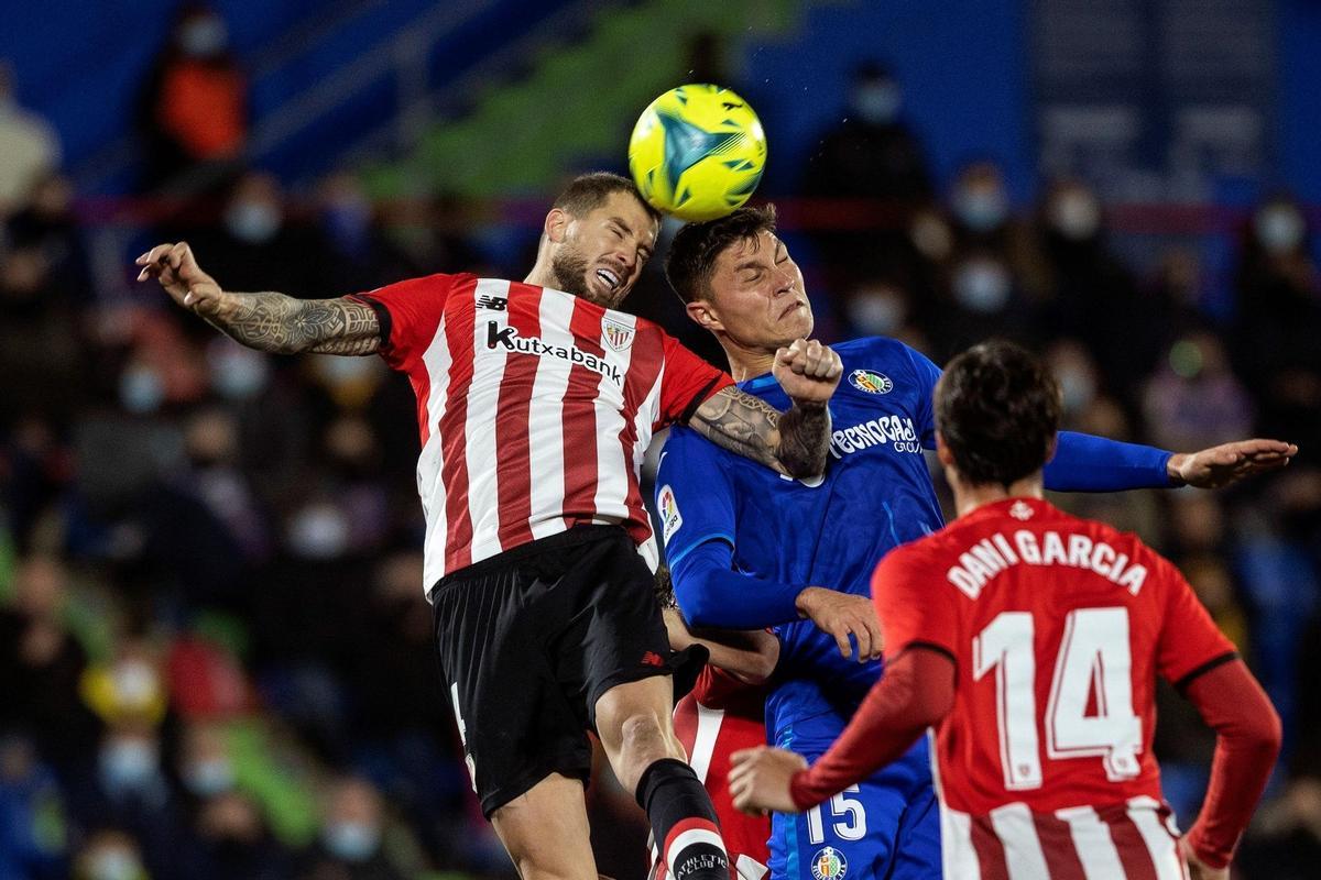 GETAFE (MADRID), 06/12/2021.- El defensa del Getafe Jorge Cuenca (c) salta a por un balón con Íñigo Martínez (i), del Athletic, durante el encuentro de la jornada 16 de LaLiga Santanter entre el Getafe CF y el Athletic Club de Bilbao disputado este lunes en el Coliseum Alfonso Pérez de Getafe, en Madrid. EFE/Rodrigo Jiménez