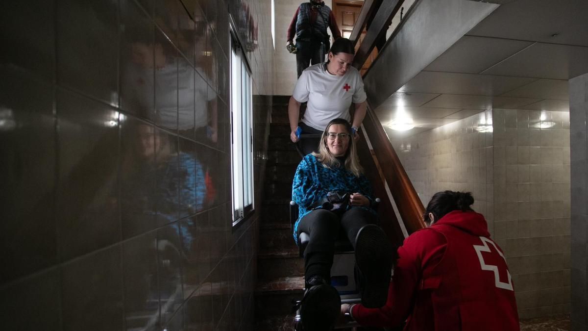 Carol baja las escaleras de su edificio en Catarroja con ayuda de dos trabajadoras de Cruz Roja