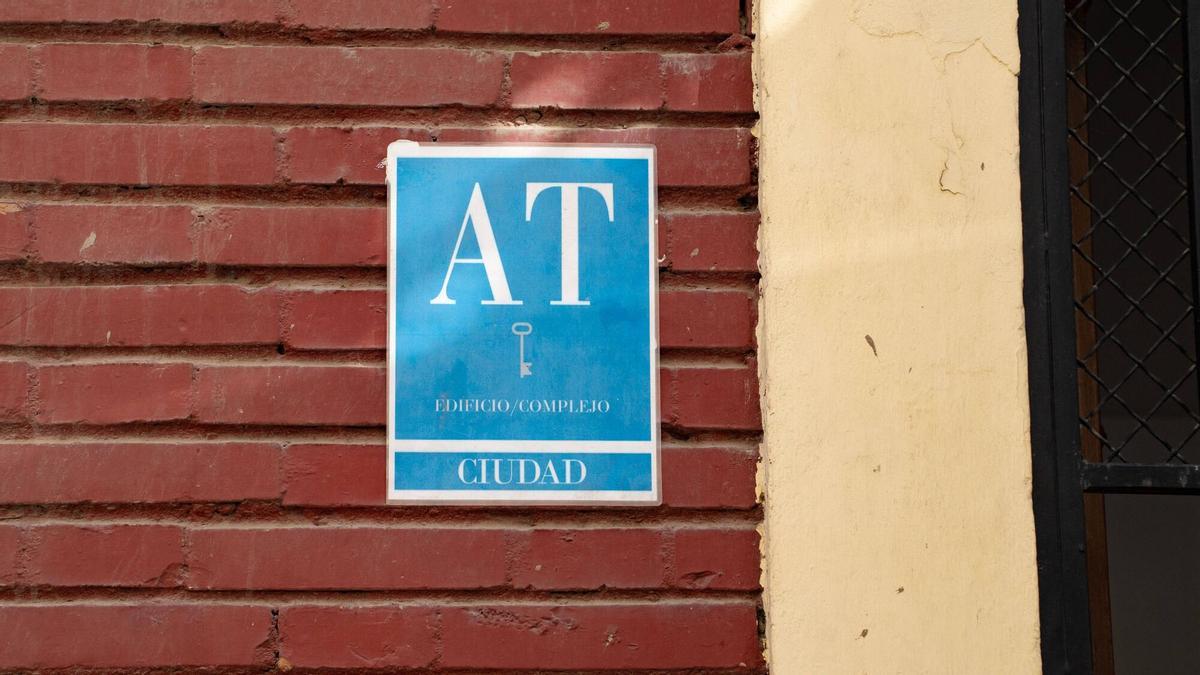 Cartel con las siglas ‘AT’ en la fachada de un edificio, correspondiente a "apartamento turístico".