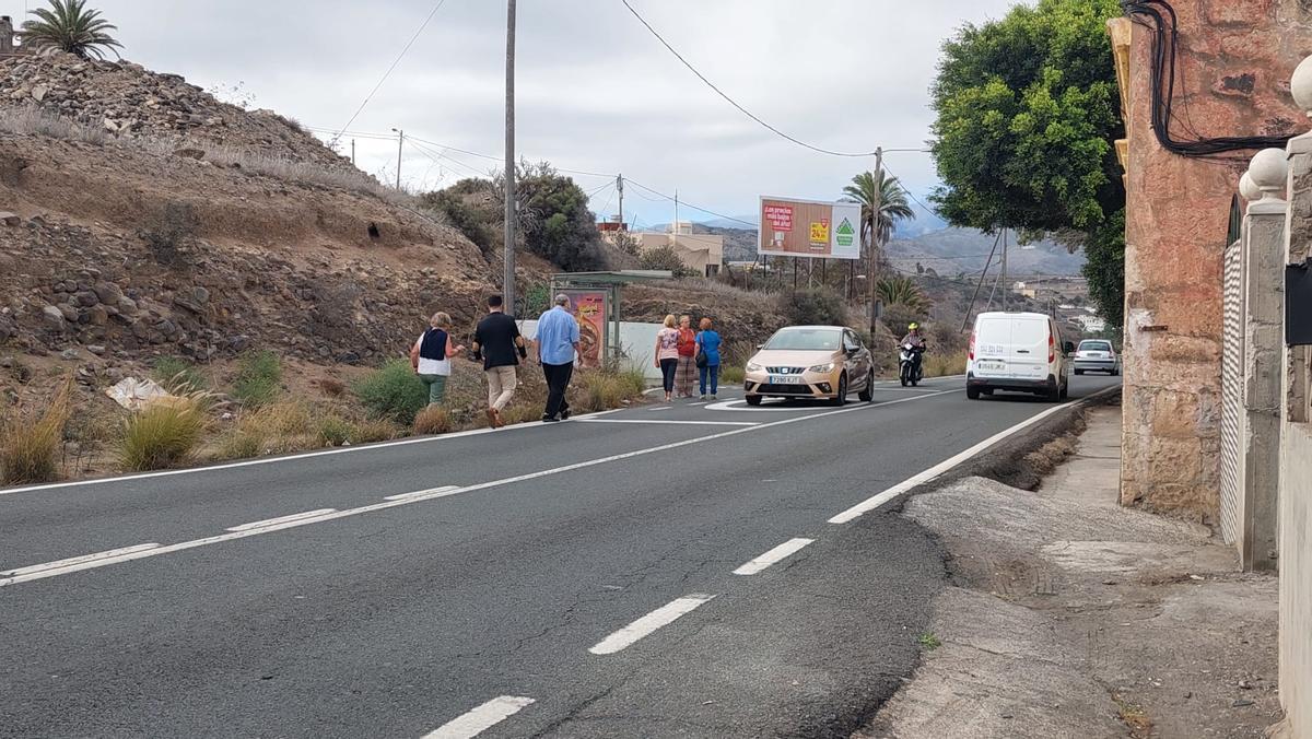 Vecinas y vecinos de Las Perreras caminan a un lado de la carretera para coger la guagua