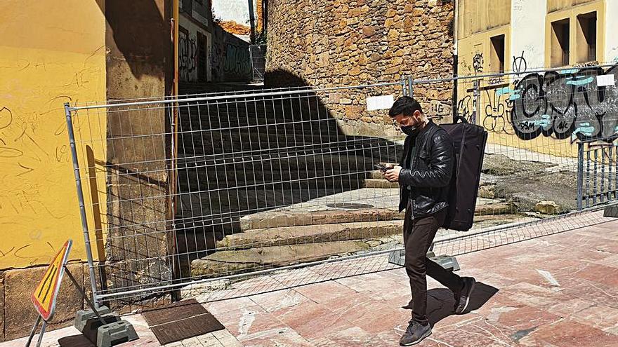 Un peatón pasa junto a la escalinata de la calle Ildefonso Martínez, vallada para el comienzo de su reparación. | LNE