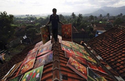 An artist walks across the roof of his house while carrying paintings to be dried at Jelekong village near Bandung