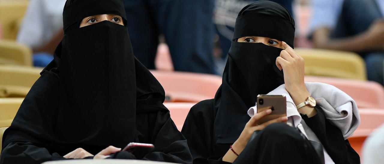 Unas mujeres viendo un partido de fútbol con un burka.