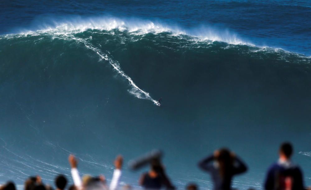 A surfer rides a large wave at Praia do Norte in ...