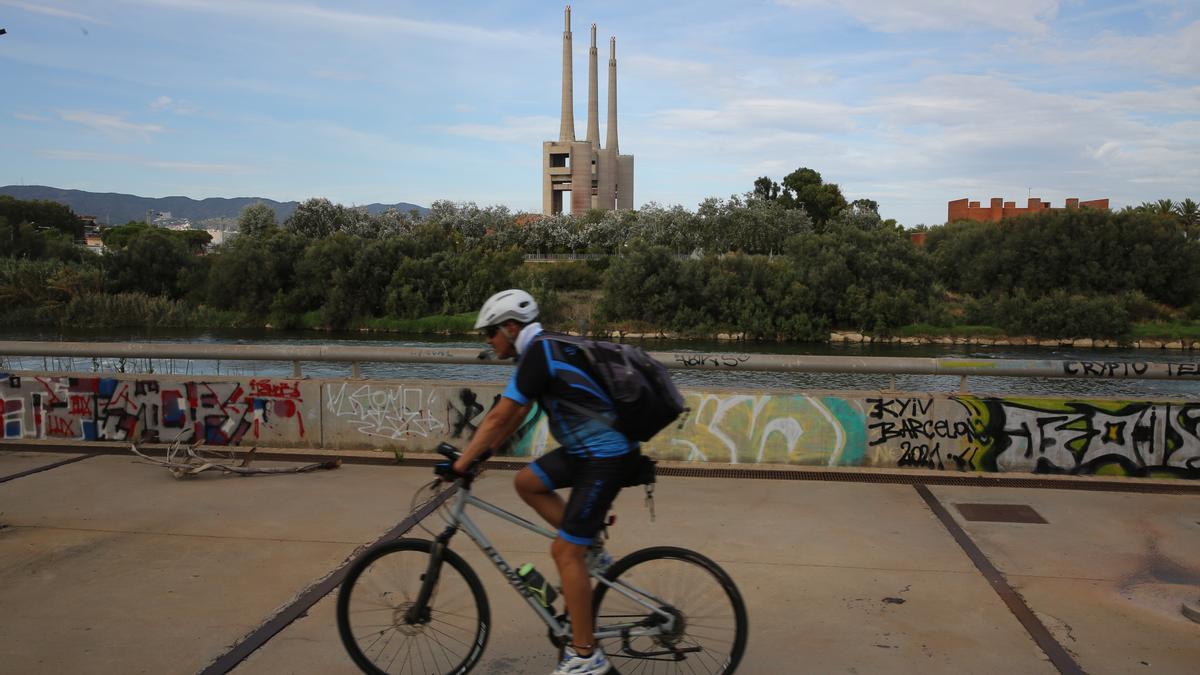 Un ciclista circula junto al río Besòs, con la antigua central térmica de las Tres Xemeneies al fondo.