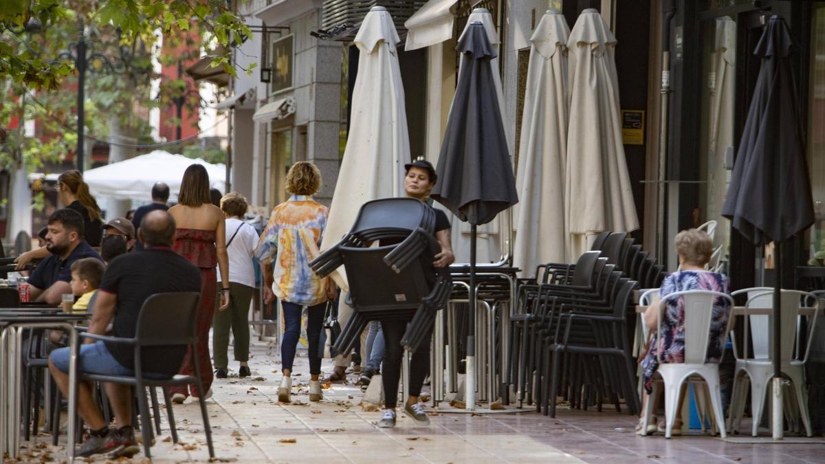 Una trabajadora transporte unas sillas en una terraza de l'Albereda de Xàtiva.