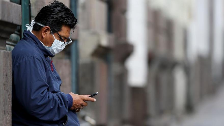 Un hombre con mascarilla mira su móvil.