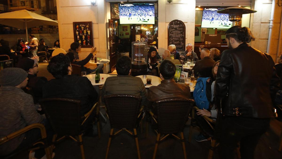 Personas ven un partido de fútbol en la terraza de un local