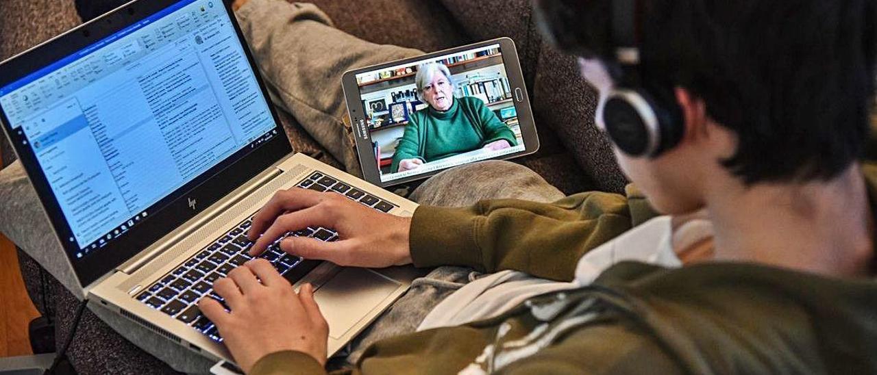 Un estudiante sigue una clase por internet en su casa frente a su ordenador y tableta.