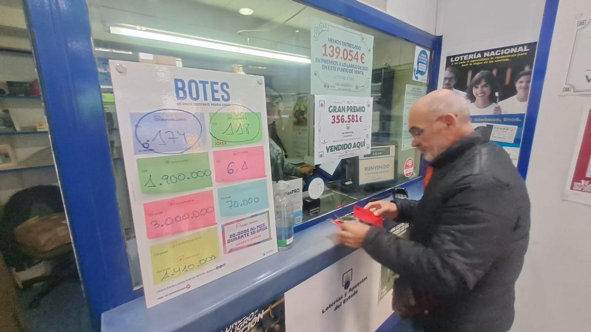 Un vecino compra lotera en la aminiatración de Santa Marina, junto al cartel que anuncia el reciente premio de la Primitiva.