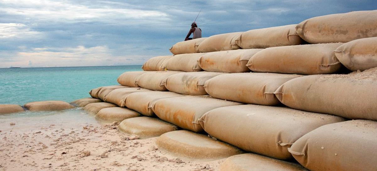 En la isla de Tuvalu, en el Pacífico, un hombre está sentado sobre sacos de arena para evitar la subida del nivel del mar