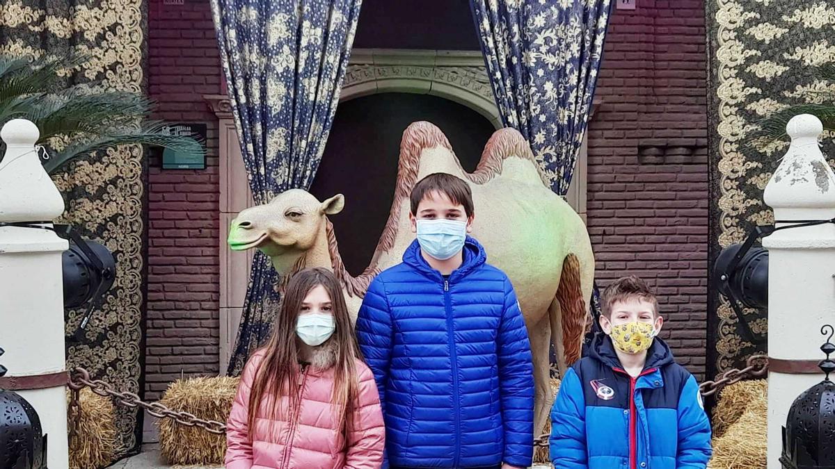Tres niños posan junto a un camello de los Reyes en el Poble Espanyol.
