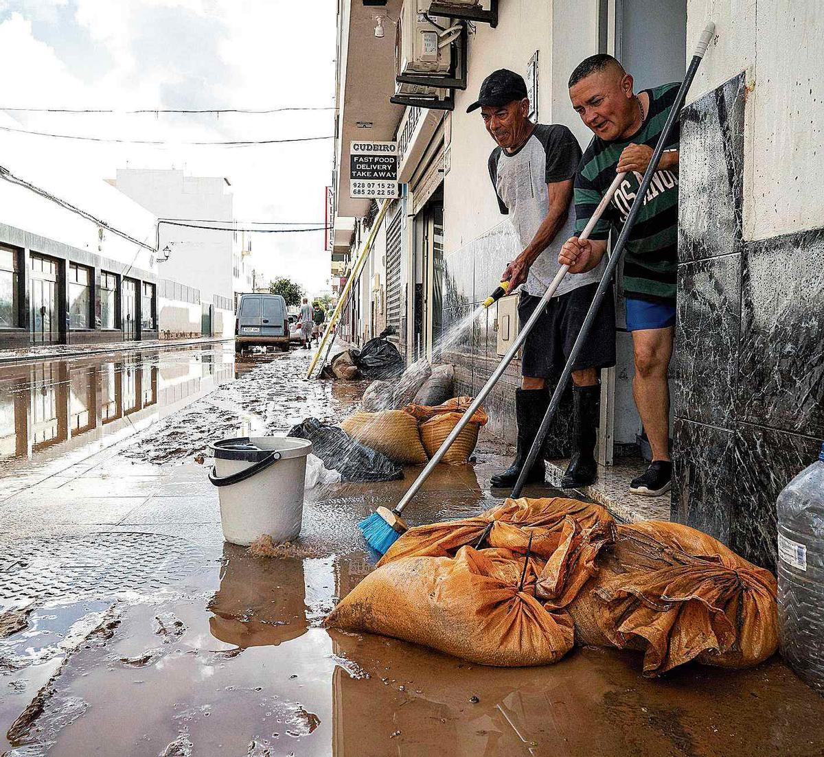 Dos residentes de Arrecife limpian las aceras al acabar el chaparrón de agua.
