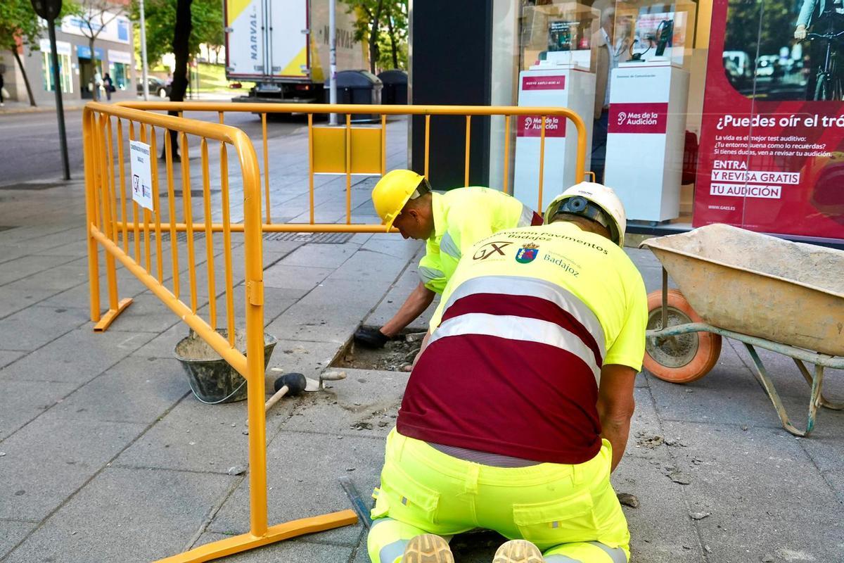 Dos obreros reparan el acerado en la confluencia de las avenidas Enrique Segura Otaño y Fernando Calzadilla de Badajoz.