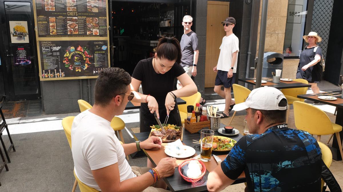 Una camarera atiende a una pareja de clientes la terraza de un restaurante
