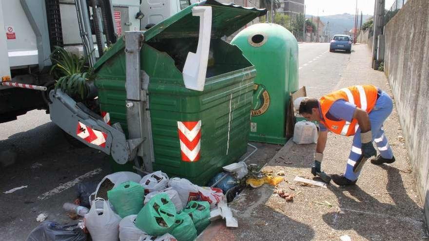 Un trabajador del servicio de recogida de basura limpia el entorno de un contenedor.  // Santos Álvarez