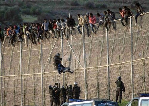 Un inmigrante africano es bajado de la valla fronteriza que separa Marruecos y España por un policía