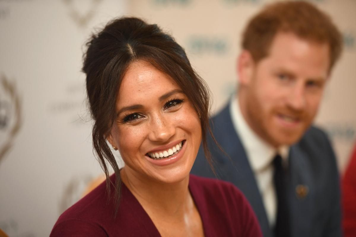 Primer plano de Meghan Markle con el principe Harry de fondo