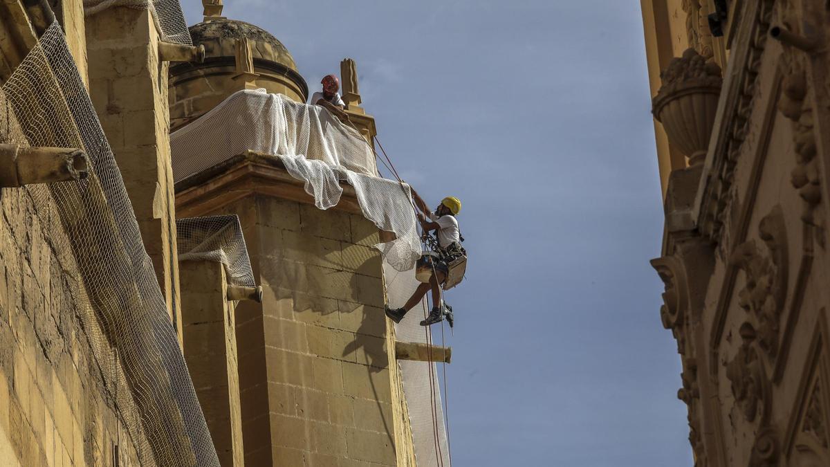 Dos operarios colocan una nueva red en una de las cornisas de Santa María, en la fachada sur, este lunes.