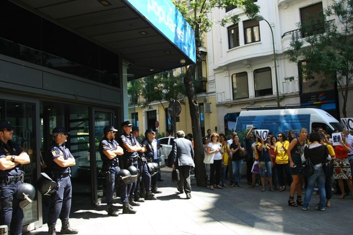 Manifestants concentrats a les portes de la seu del PP sota la vigilància dels agents de la policia.