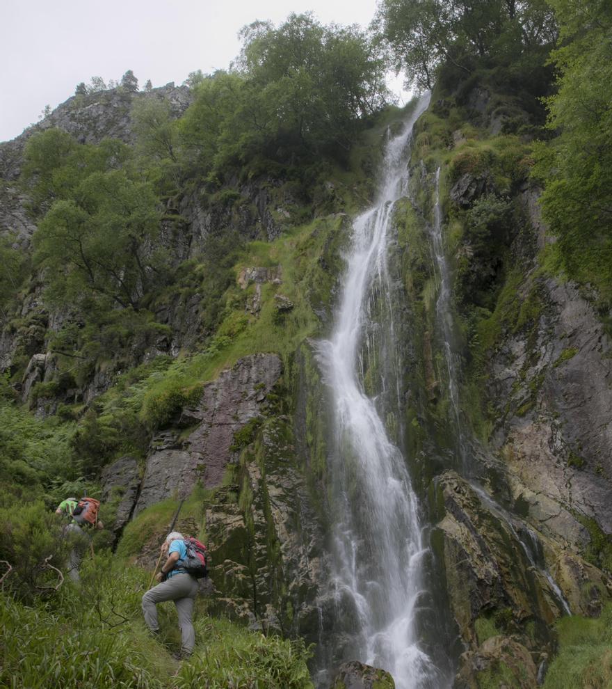 Dos visitantes junto a la cascada del Tabayón del Mongallu, en Caso, un salto de agua que también es monumento natural