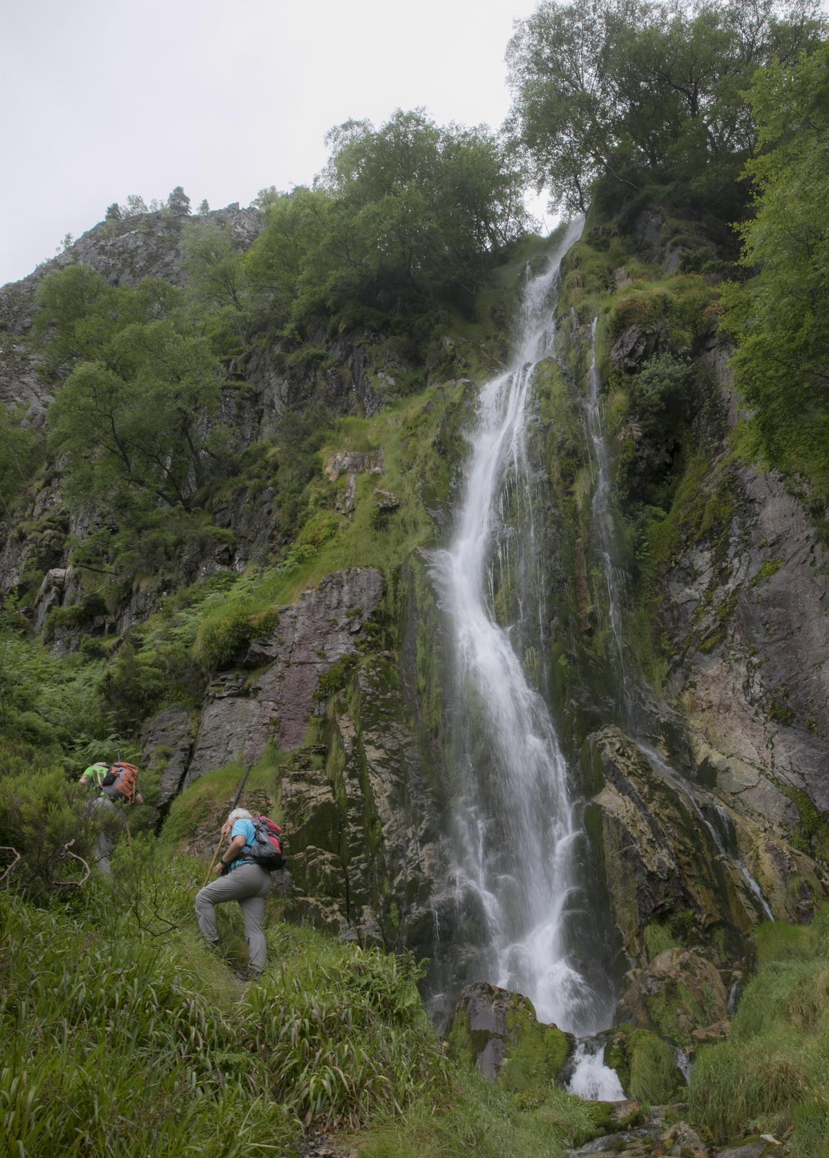 Dos visitantes junto a la cascada del Tabayón del Mongallu, en Caso, un salto de agua que también es monumento natural