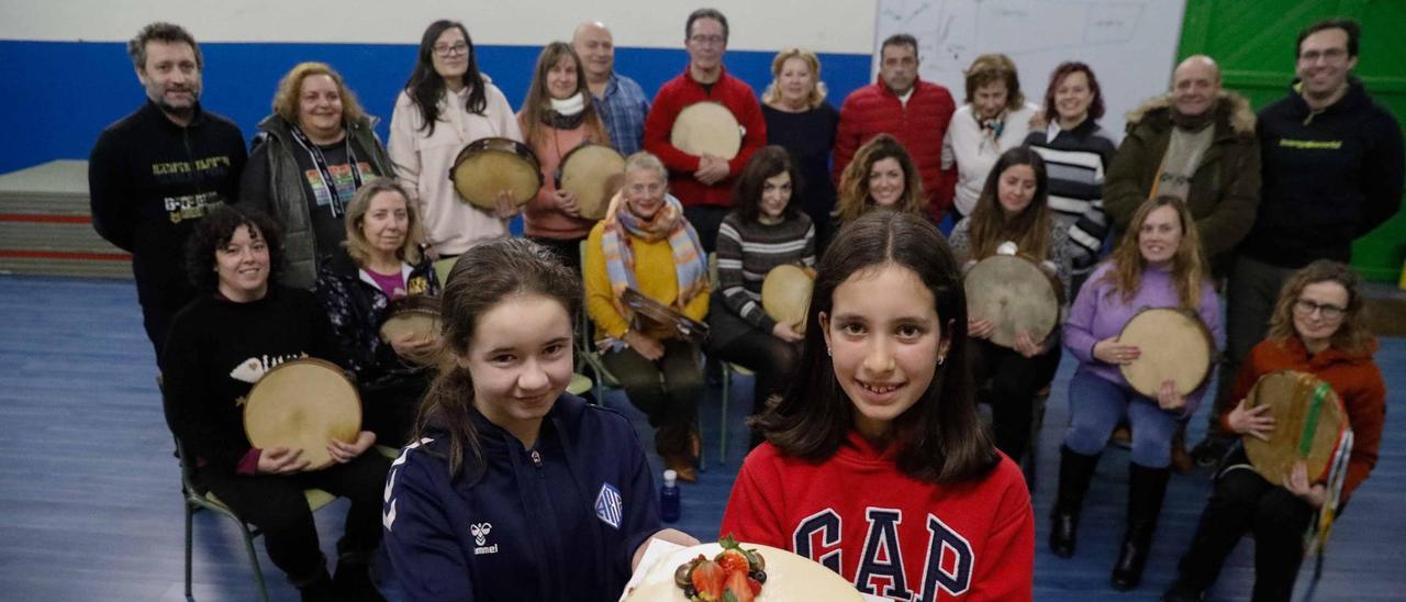 Marta Facundo y Daniela Seoane con la tarta de cumpleaños y tras ellas miembros de Esbardu y alumnado del taller de pandereta.