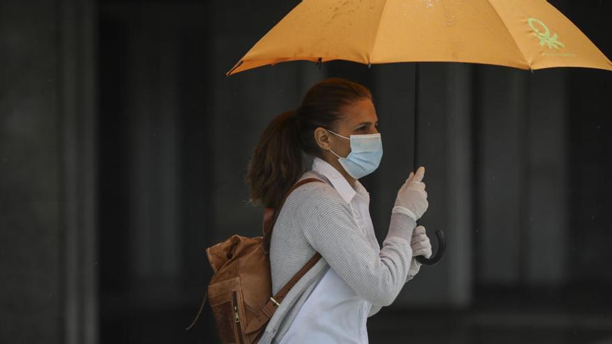 Una dona protegida amb mascareta i guants es resguarda de la pluja a Sevilla