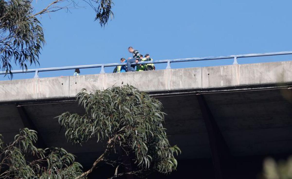 Por la izquierda, el hombre, ayudado, baja de la barandilla del puente de la autopista; ya sujetado, es trasladado por un agente, y, a la derecha, corte del tráfico a la altura de La Consolación. | M. V.