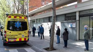 Varias personas hacen cola respetando la distancia de seguridad para entrar en un ambulatorio, junto a una ambulancia del SEM, en Barcelona.