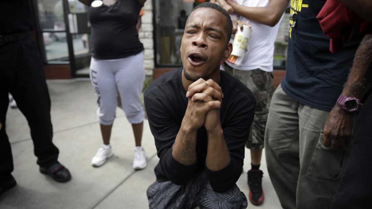 Un hombre reza mientras la policía dispersa a los manifestantes en Ferguson tras el asesinato de Michael Brown.