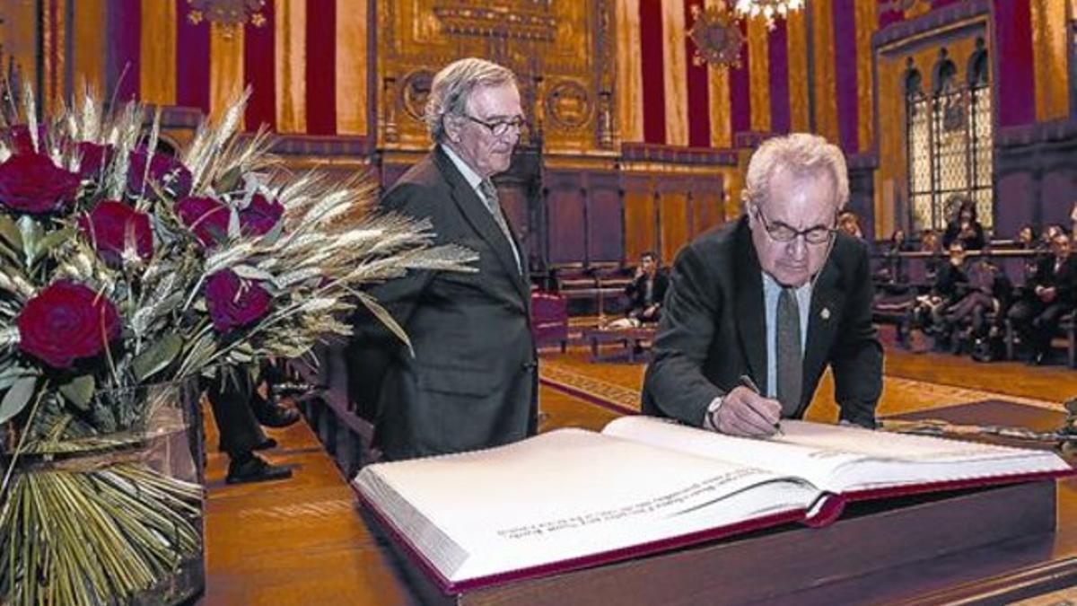 Banville firma el libro de honor del Ayuntamiento de Barcelona ante la mirada de Xavier Trias.