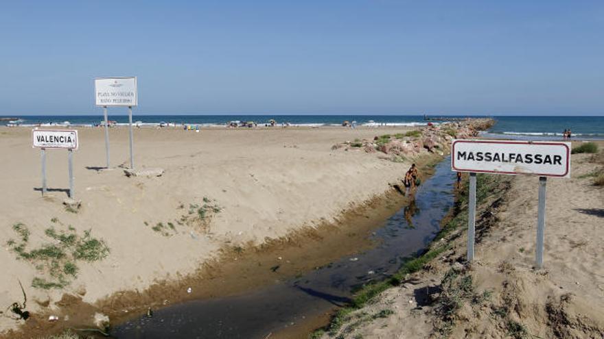 Una acequia marca los lindes municipales en la playa de Rafalell donde un cartel desaconseja el baño.