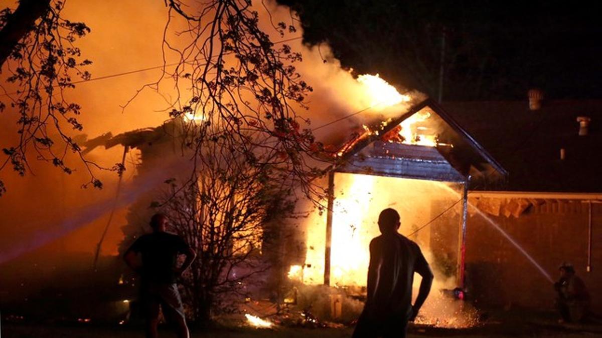 Un vecino observa el trabajo de los bomberos para apagar el fuego de una casa afectada por la explosión.