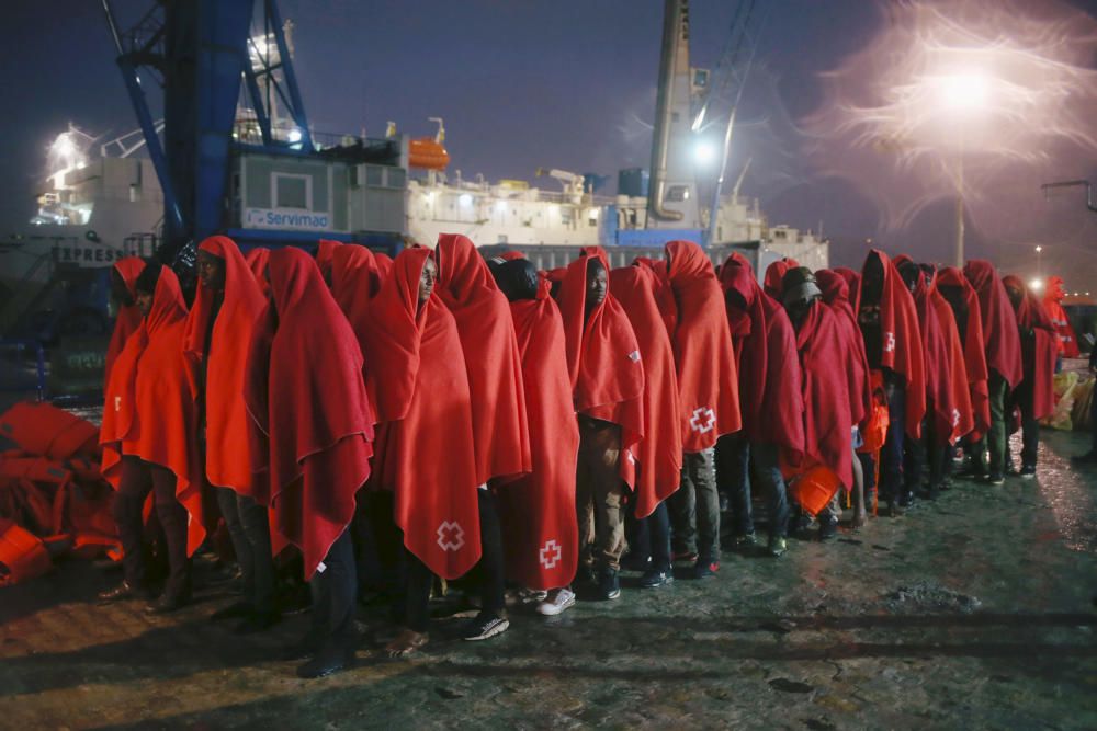 Migrants stand under the rain after disembarking ...