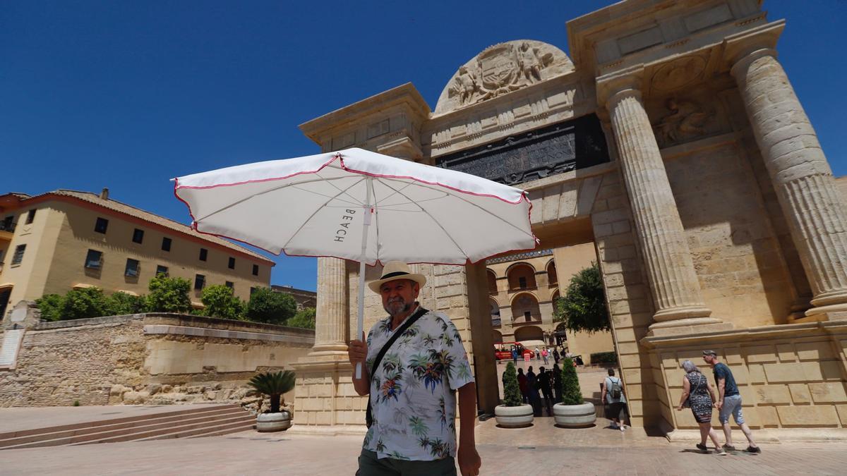 Un turista se protege del sol con una sombrilla en la Puerta del Puente.