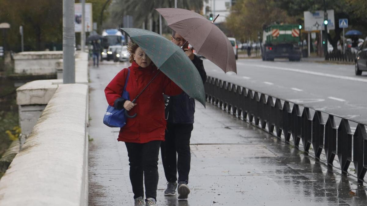 Dos personas se protegen con paraguas de la lluvia, por el puente de San Rafael, en una imagen de archivo