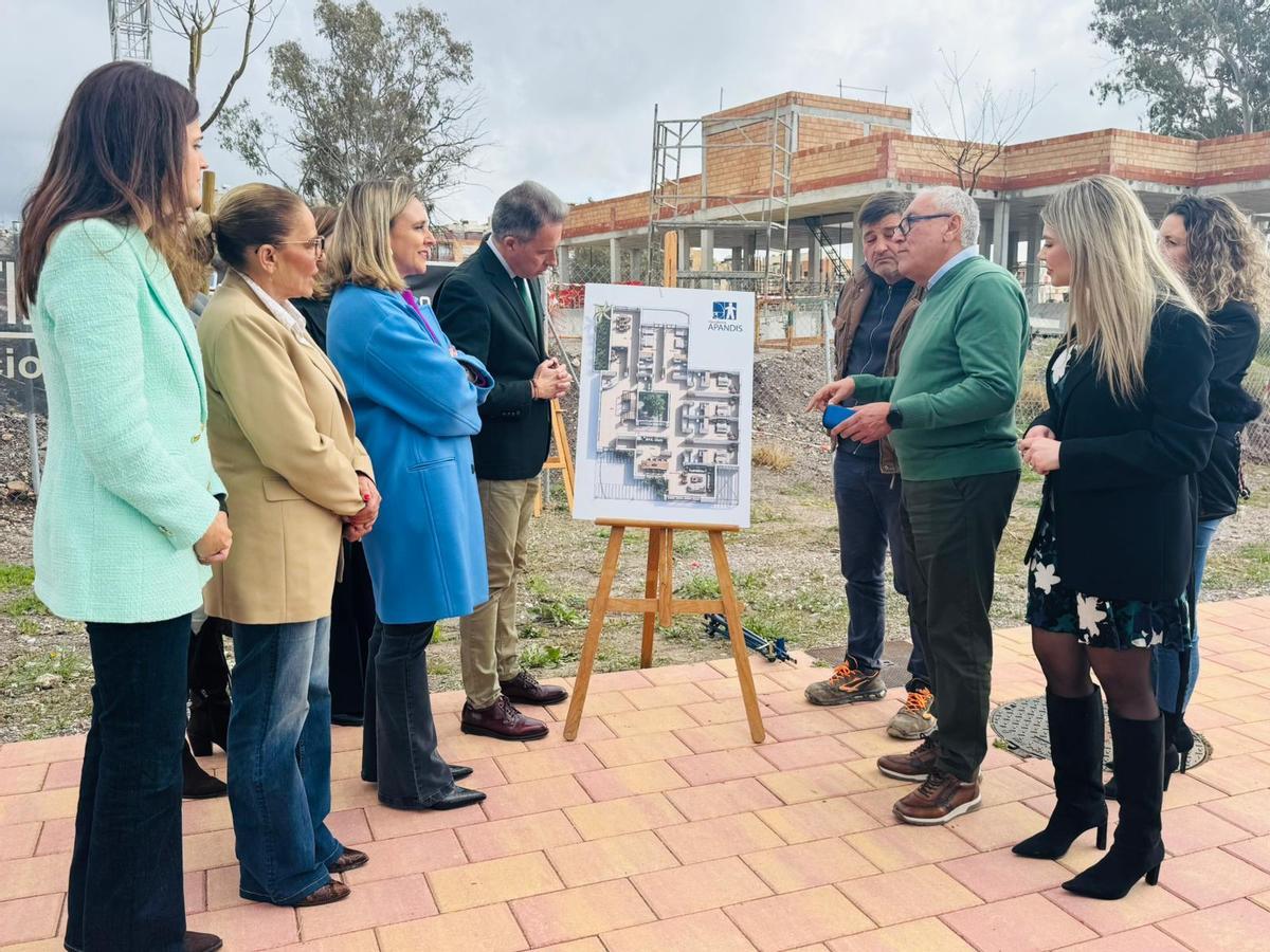 Los participantes en la visita contemplan los planos, con el nuevo edificio al fondo.