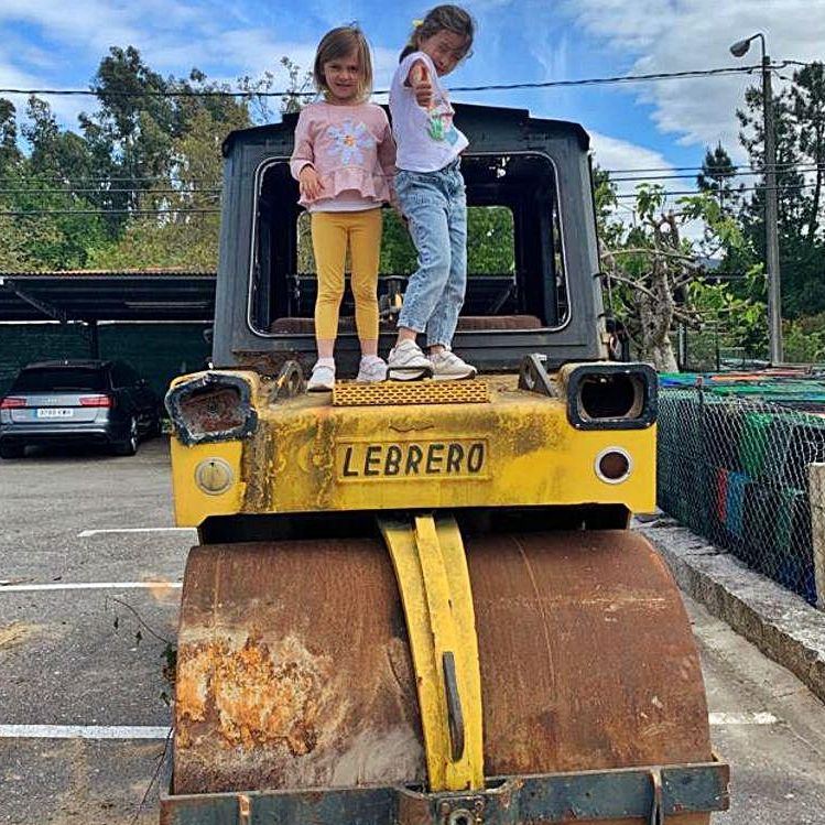 Dos niñas sobre la apisonadora que las familias restauran para el patio. 