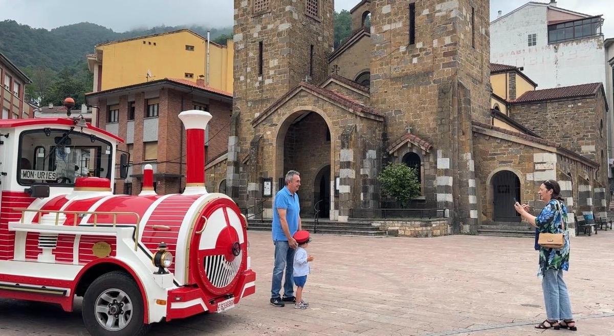 Un niño con la gorra del maquinista posa con el tren turístico de Aller