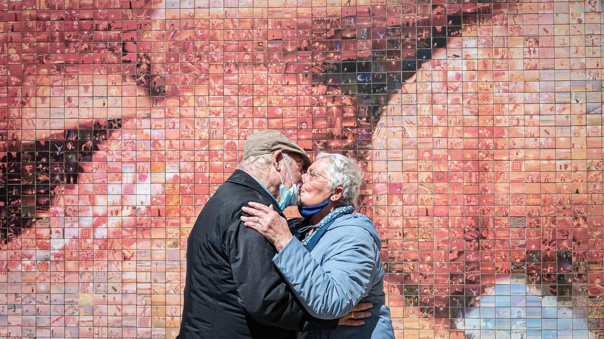 Dos mayores se besan frente a un mural en Barcelona.