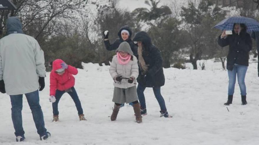 Un grupo de personas en un terreno cercano al cementerio de Alcoy tirándose bolas de nieve y haciendo fotografías con la cámara del móvil.