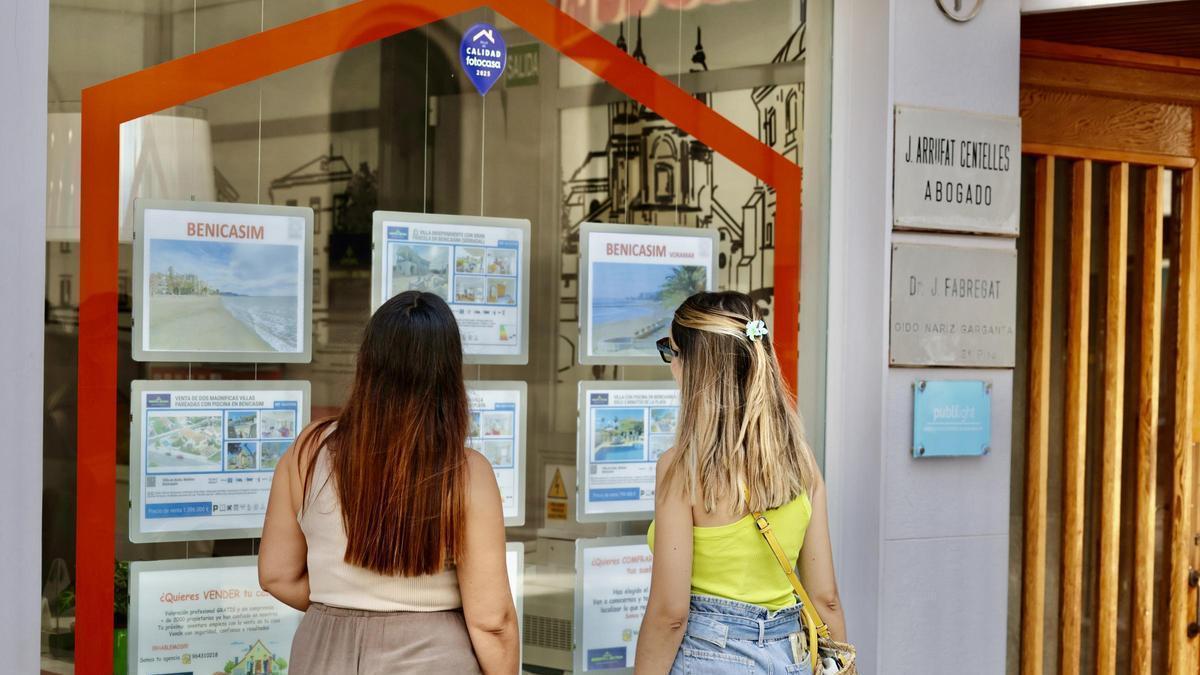 Dos jóvenes miran el escaparate de una inmobiliaria en Castelló.