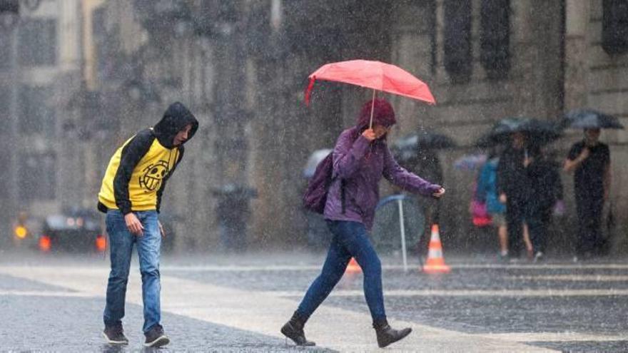 Dos joves creuen la plaça Sant Jaume de Barcelona, dijous, sota la pluja abundant.