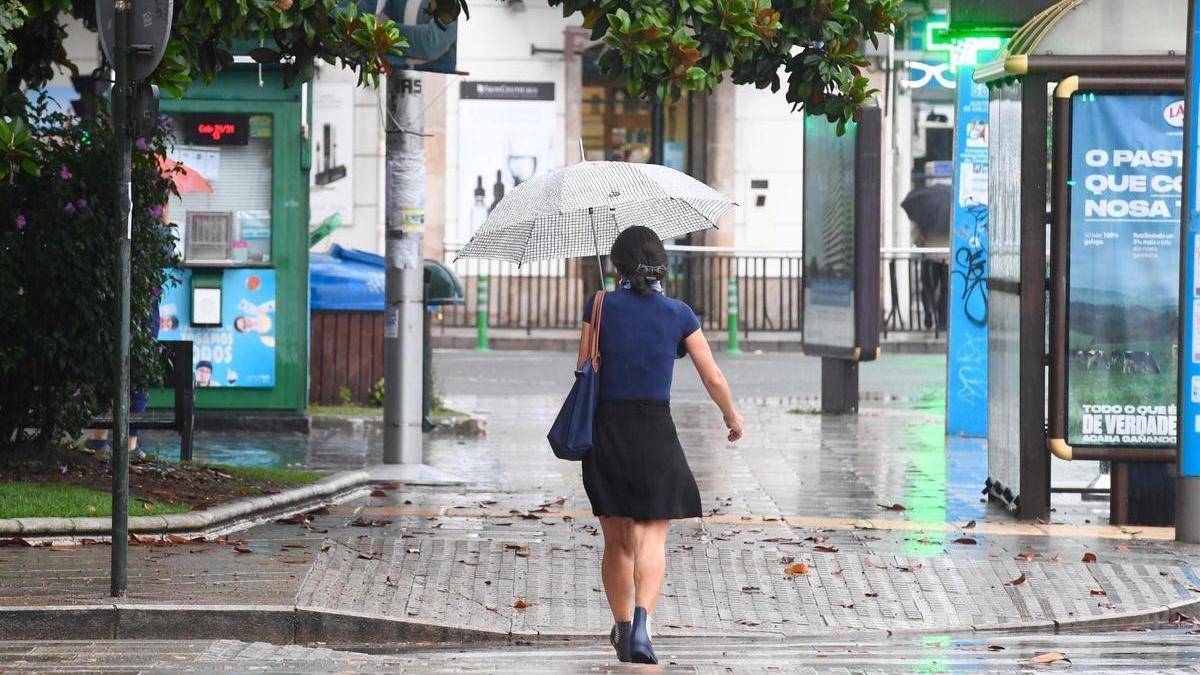 Una mujer cruza con un paraguas un paso de peatones en la plaza de Ourense de A Coruña.