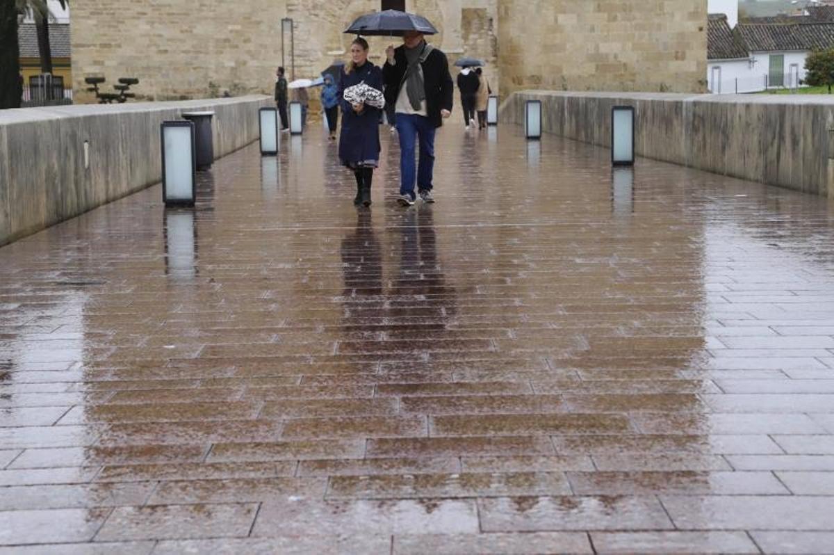 Dos personas pasean por el Puente Romano bajo un paraguas.