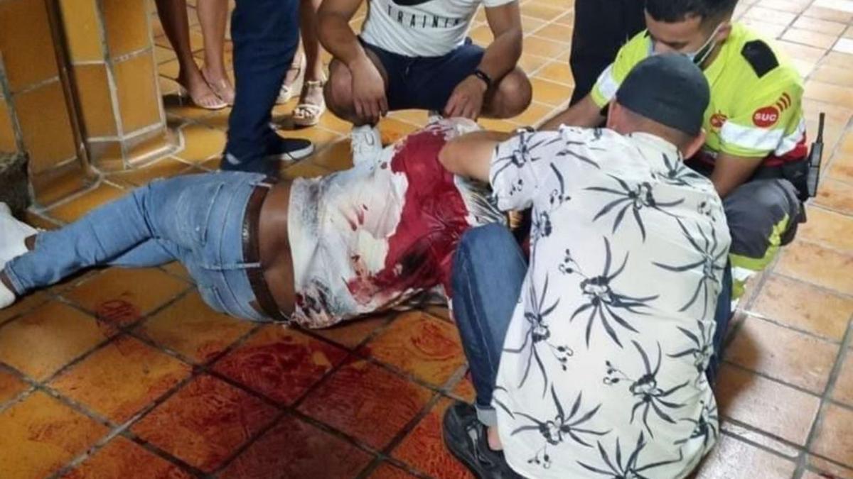 Un hombre ensagrentado en el suelo recibe asistencia de un miembro del SCS y otras personas, en Corralejo.